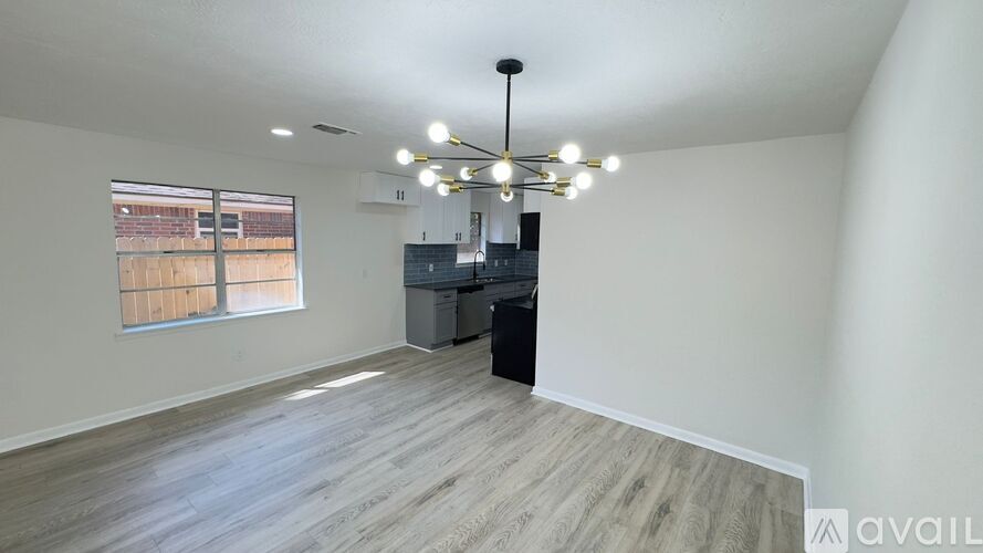 A spacious room with a large window, wooden flooring, and a chandelier hanging from the ceiling.