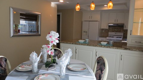 A dining table set with plates and glasses with a view of the kitchen in the background.