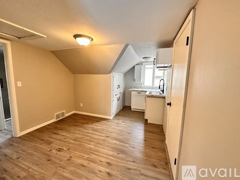 A kitchen area with a sink, stove, and refrigerator in a room with wooden flooring.