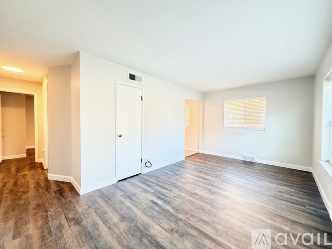 A spacious room with wooden flooring and white walls.