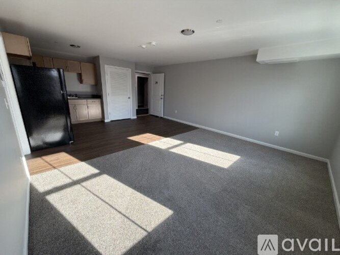 A spacious room with a black fridge and a carpeted floor.
