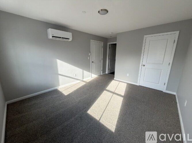 A room with a carpeted floor, two doors, and an air conditioner unit on the wall.