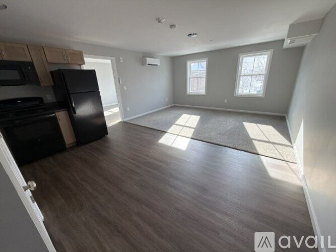 A spacious empty room with wooden flooring and a kitchen area to the left.