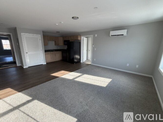 A spacious room with a rug on the floor and a kitchen area in the background.