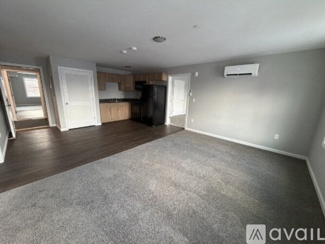 A spacious living room with a kitchen in the background and a carpet on the floor.