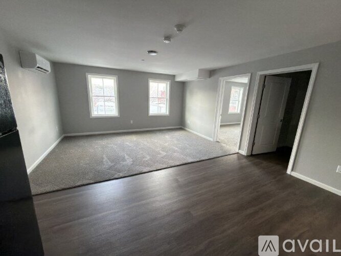 A spacious room with wood flooring and three windows.