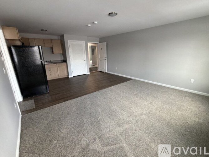 A spacious living room with a black fridge and carpeted floor.