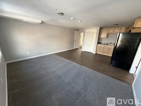 A spacious room with a black fridge and wooden cabinets.
