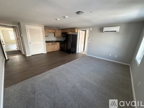 A spacious living room with a grey carpet and a kitchen in the background.