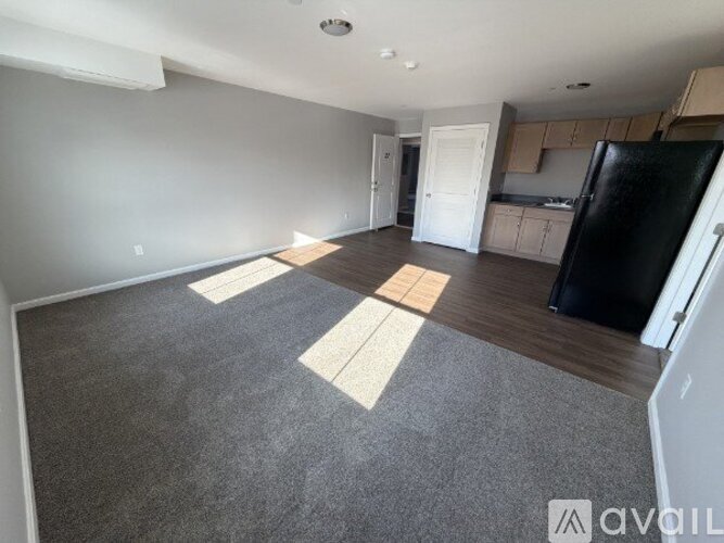 A spacious living room with a black refrigerator and wooden flooring.