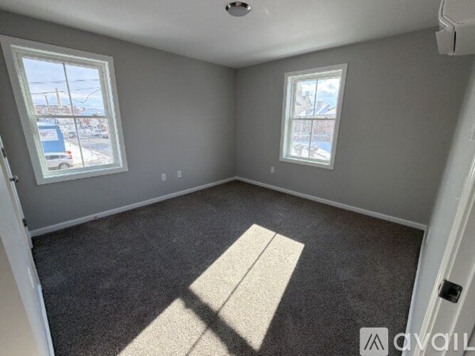 A room with grey walls and carpet flooring, two windows, and a door.