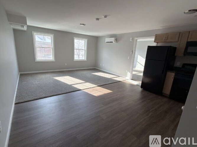 A spacious room with wooden flooring and a black refrigerator.