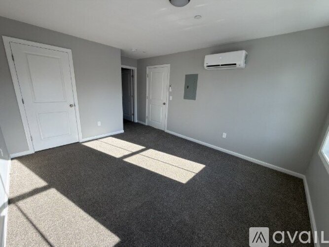 A room with a carpeted floor, two doors, and an air conditioner unit on the wall.