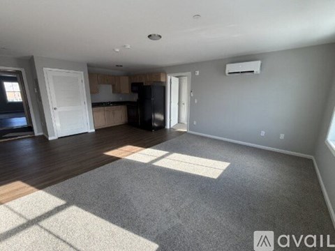A spacious room with a rug on the floor and a kitchen area in the background.