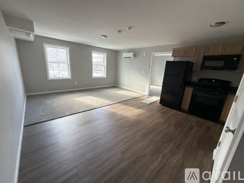 A spacious room with wooden flooring and a black refrigerator.