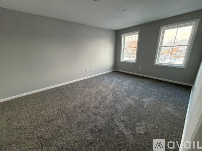 A room with grey carpet and two windows.
