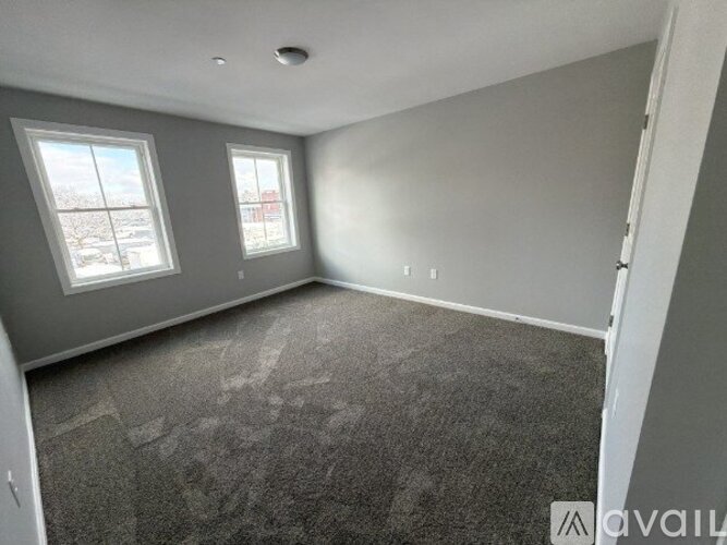 A room with grey carpet and two windows overlooking a cityscape.