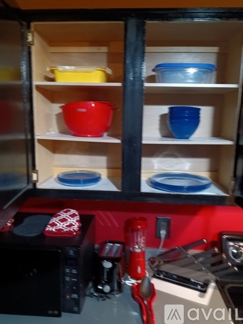 A kitchen cabinet with a red pot on the bottom shelf.