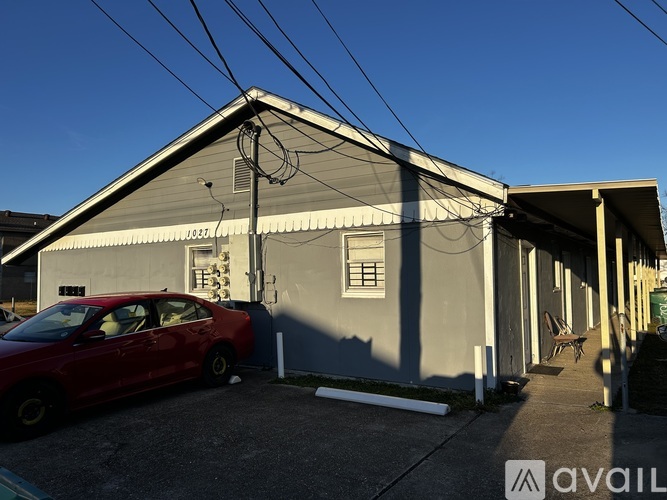 A red car is parked in front of a grey building with a sign that reads "AVAIL".