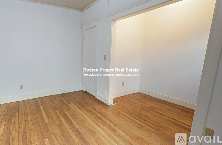 A room with wooden flooring and a doorway leading to another room.