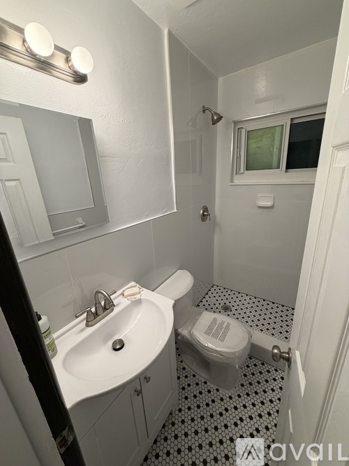 A bathroom with a toilet, sink, mirror and a window.