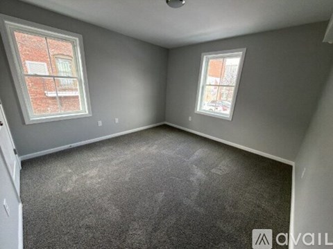 A room with grey carpet and two windows.