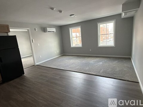 A spacious room with a black refrigerator and two windows.