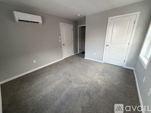 A room with grey carpet and white walls with an air conditioner on the wall.