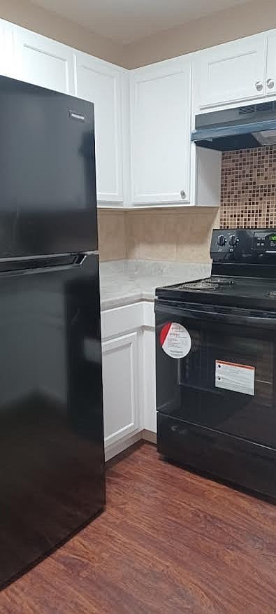 A black fridge and stove in a kitchen with white cabinets.