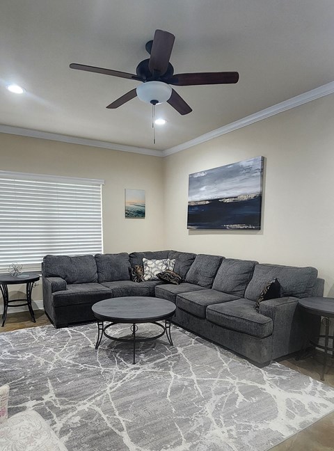 A living room with a grey sectional sofa, a round coffee table, and a ceiling fan.