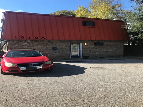 A red car is parked in front of a building with the number 1610A on it.