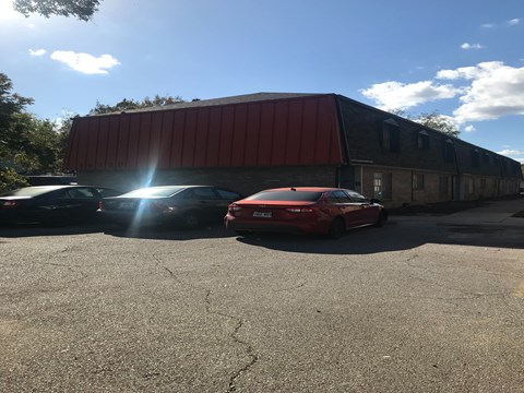 A red car is parked in front of a building with a red roof.