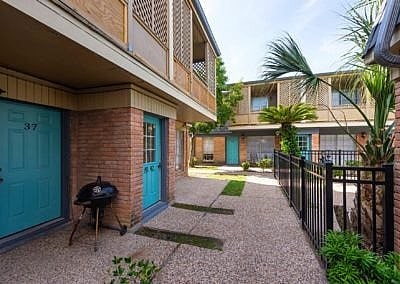 A patio with a BBQ grill is surrounded by a black fence.