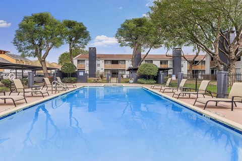 A swimming pool surrounded by trees and chairs.
