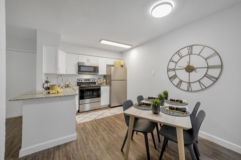A kitchen with a table set for two and a clock on the wall.