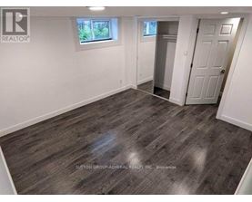 A room with wooden flooring and white walls, with a door leading to another room.