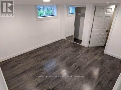 A room with wooden flooring and white walls, with a door leading to another room.