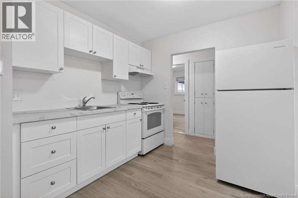 A white kitchen with wooden floors and a refrigerator on the right.