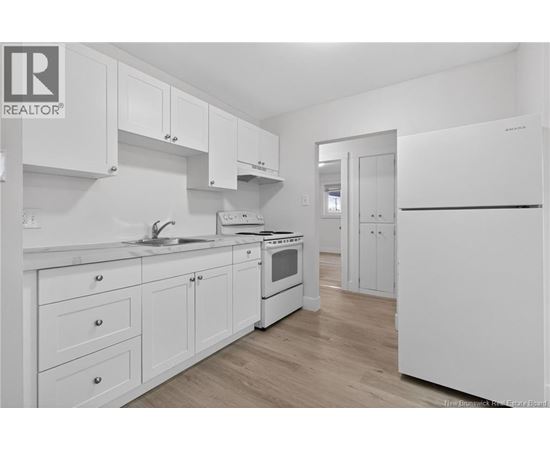 A white kitchen with wooden floors and a refrigerator on the right.