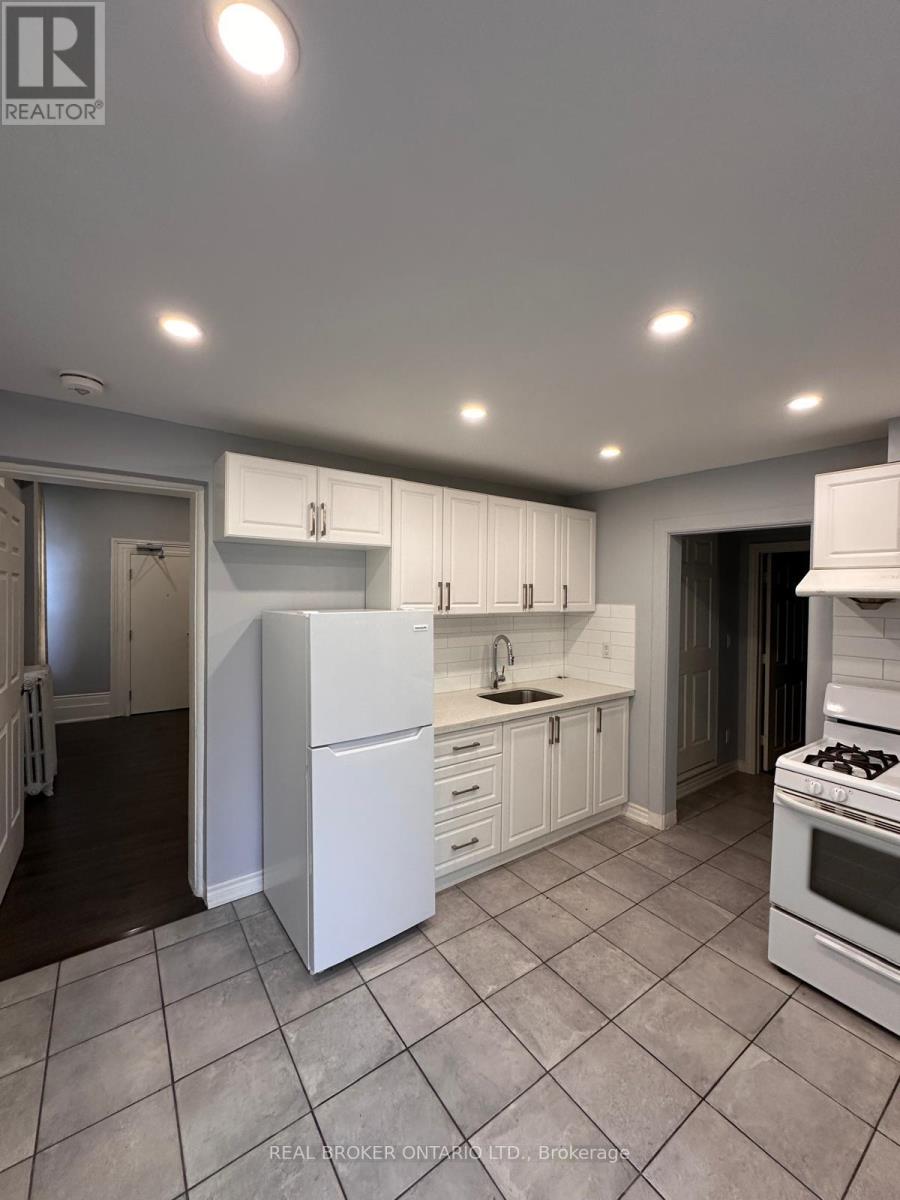 A white kitchen with a refrigerator, sink, and stove.