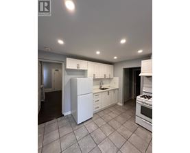 A white kitchen with a refrigerator, sink, and stove.