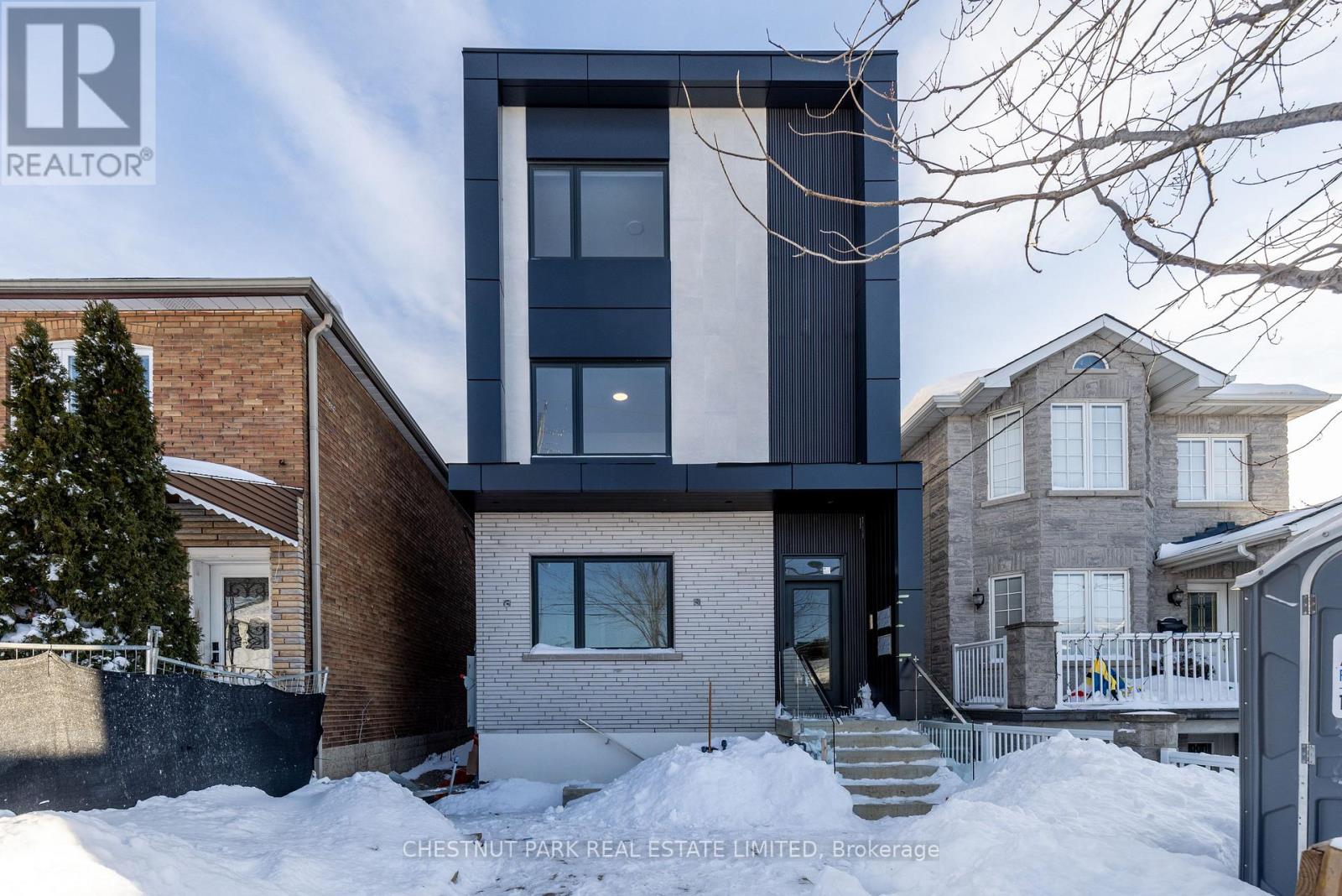 A modern house with a black and white exterior is surrounded by snow.