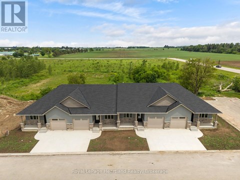 A large, two-story house with a grey roof and a white garage door is surrounded by a grassy field.