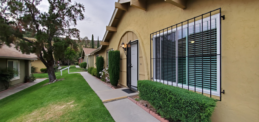 A yellow house with a black gate and a green bush.