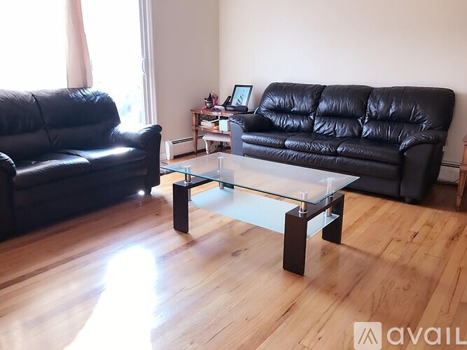 A black leather couch sits in a living room with a glass coffee table in front of it.
