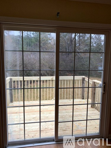 A sliding glass door with a view of a deck and trees outside.