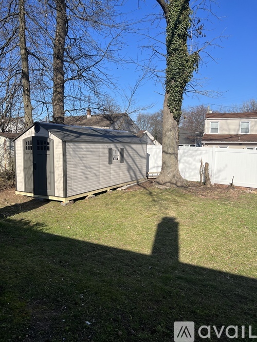 A small, grey, single-story building with a dark grey door and a small window is situated in a grassy area.