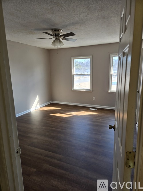A room with a ceiling fan and two windows.