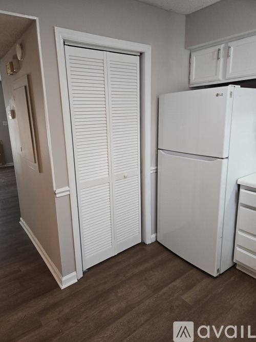A white refrigerator in a kitchen with wooden flooring.