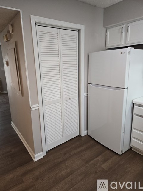 A white refrigerator in a kitchen with wooden flooring.